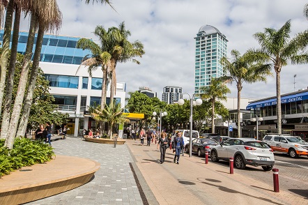 Takapuna's main street showing pedestrians, cars and palm trees.